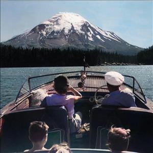 Two adults, three kids, and a dog all facing away from camera, in a boat pointing towards a snow-capped mountain
